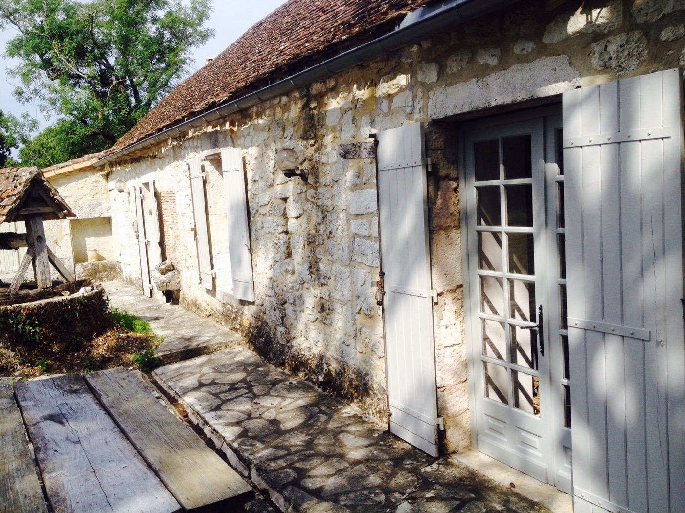 Historic stone façade, pale shutters and old well at Le Petit Capelier